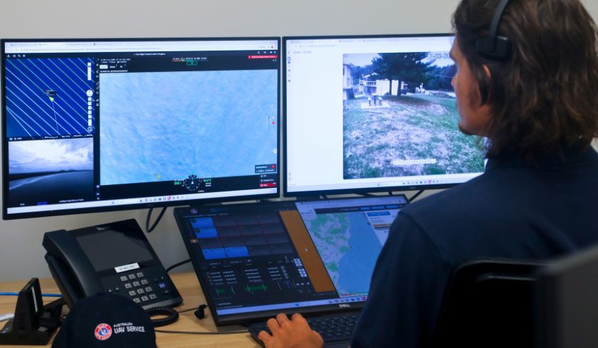 UAV operator seated at a desk monitoring multiple screens showing aerial maps, live drone footage, and flight data.