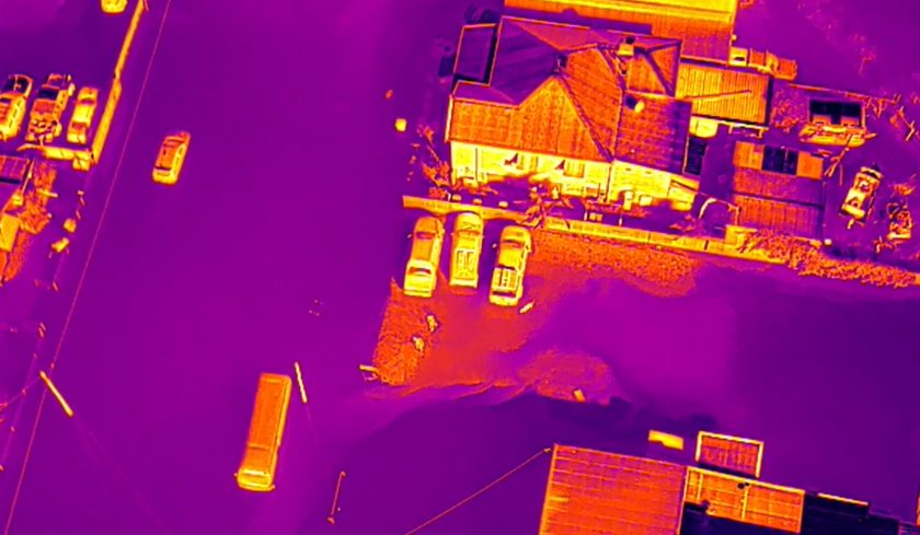 Thermal aerial image showing flooded buildings, vehicles, and roads in contrasting heat-map colours.