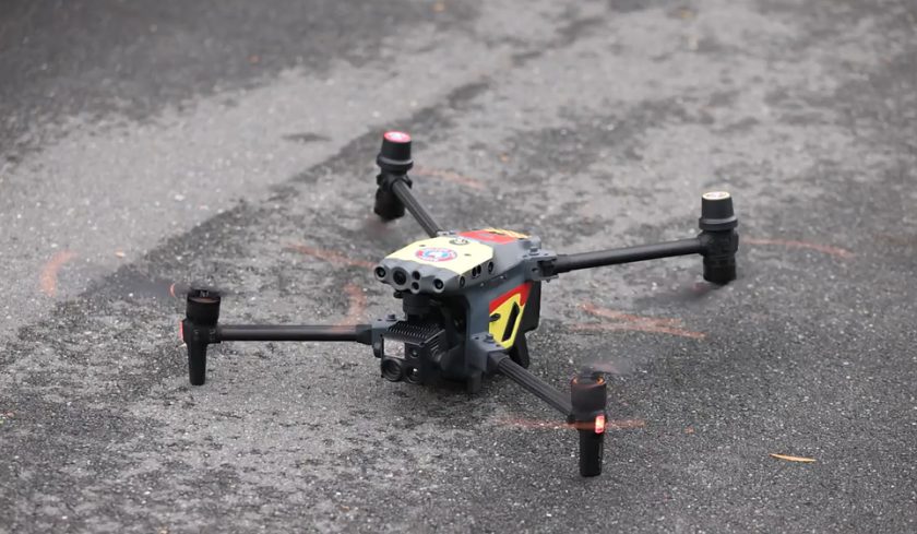 Close-up of a quadcopter drone resting on wet asphalt, with camera and sensors visible.